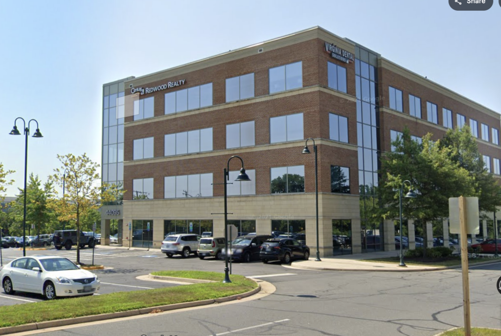 Botox, Dysport, Daxxify & Xeomin in Ashburn VA | Mountcastle Medical Spa - Mountcastle Medical Spa and Laser Center Three-story brick office building with large glass storefront windows, signage for Redwood Realty and Virginia Dental Solutions, in a parking lot with cars and street lamps.